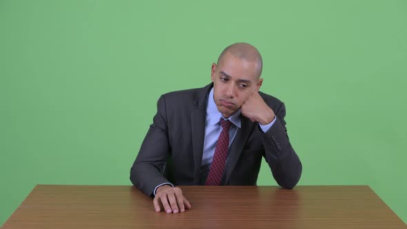 Stressed Bald Multi Ethnic Businessman Looking Bored and Tired Behind Desk