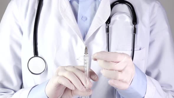 Doctor in Medical Gloves Holding Syringe and Stethoscope, on White