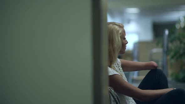 Panning slow motion shot of teenage girl sitting by locker missing part of left arm.