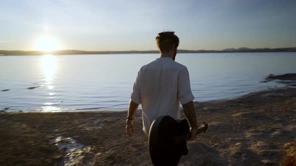 A Young Man with a Guitar Walking By the Torrevieja Pink Lake Against the Sun at Sunset Alicante