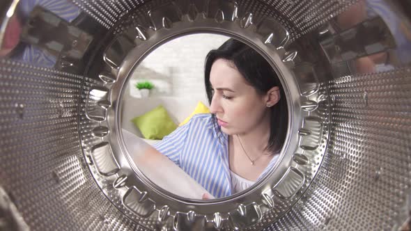 Surprised Young Woman Takes Out Laundry with a Stain From the Washing Machine