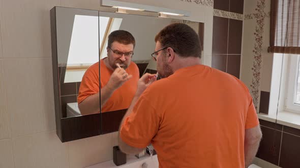 Close up head shot mirror reflection man brushing teeth with toothpaste.