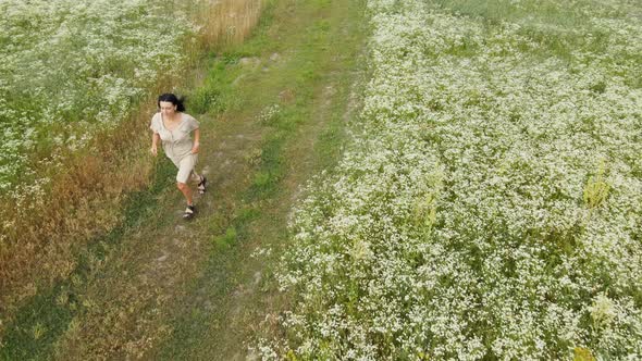 Drone aerial view of happy woman in dress running in flower blooming meadow