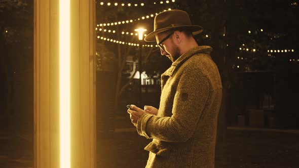 A Man in a Coat and Hat Uses a Smartphone