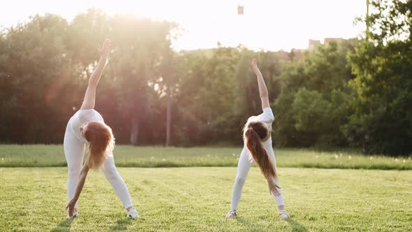 Pretty Mother and Daughter Are Doing Exercises on the Lawn