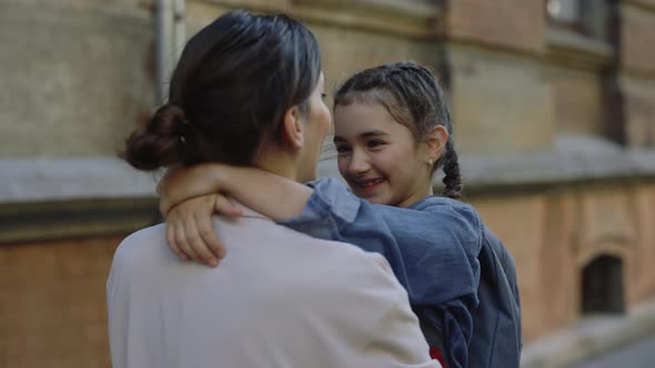 Young Mother Embraces My Daughter with a Backpack and Carrying Her in His Arms Home From School