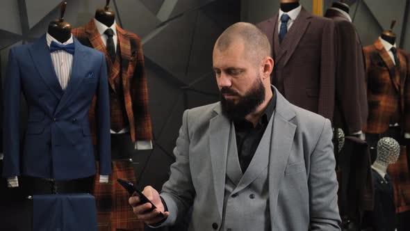 Mature Businessman with Beard Standing in a Tailor Shop Using Cell Phone and Looking at Camera