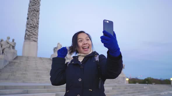 Happy Asian woman standing and taking video call in public Frogner park, Norway