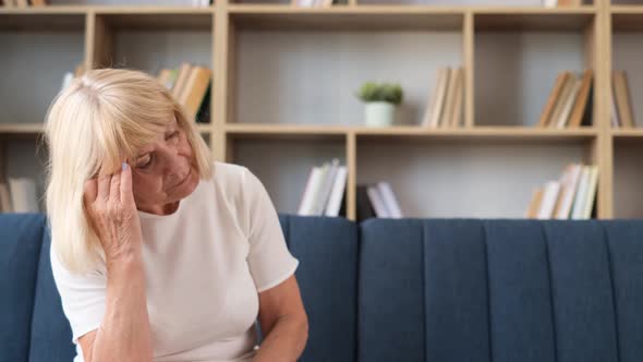 Sad Elderly Woman Grandmother Sitting on Sofa in Living Room and Suffering From Headache