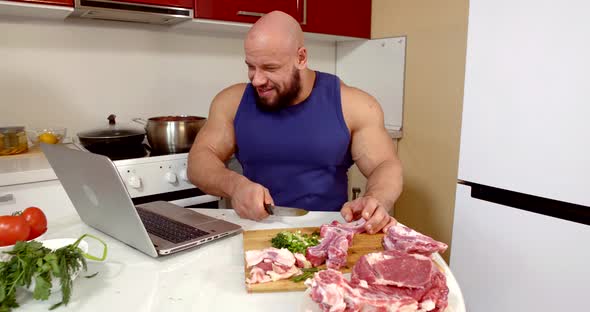 Brawny Man Is Slicing Meat and Watching Cinema on Laptop, Sitting at Kitchen Alone in Weekend