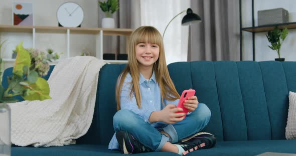 Girl in Blue Shirt and Jeans which Sitting in Relaxed Pose on Couch at Home and Looking at Camera