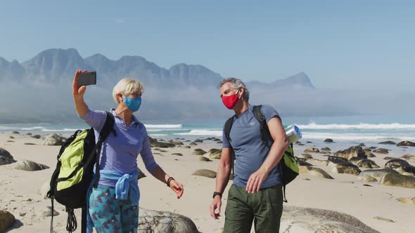 Senior hiker couple wearing face masks with backpacks waving while having a videocall on smartphone 