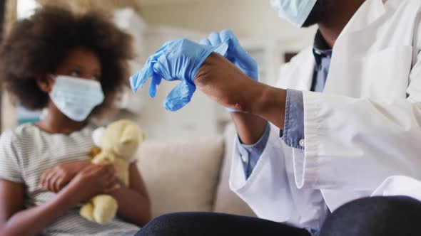 African american doctor in face mask wearing surgical gloves at home