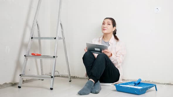 Brunette Sits By Wall and Searches Interior Design on Tablet