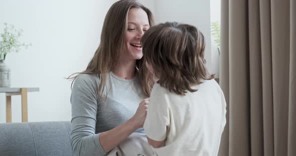 Blissful Joyous Happy Son Jumping Fun Playing and Embracing Young Mother Sitting on Couch