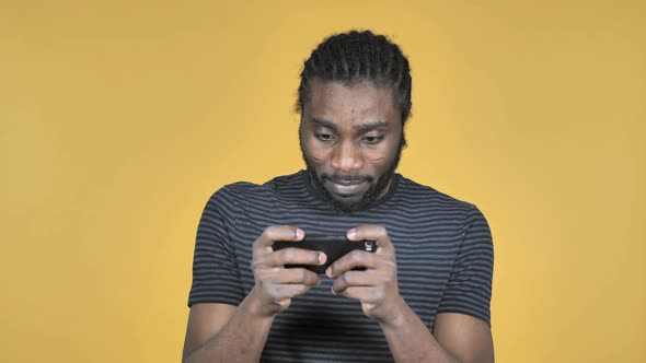 Casual African Man Playing Game on Smartphone Isolated on Yellow Background