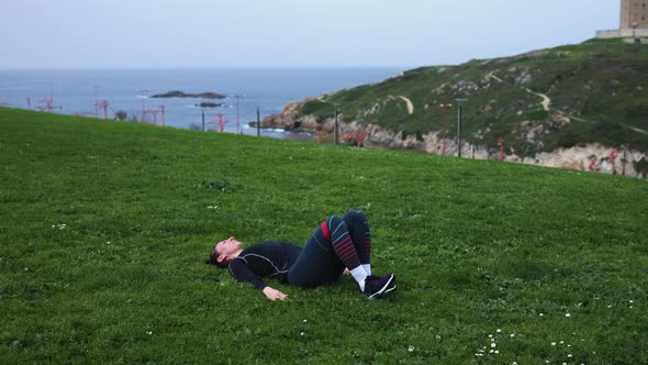 a Girl in Blue Leggings Lying on Green Grass and Doing Exercises with Rubber for the Buttocks