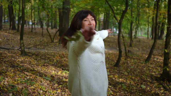 Excited Carefree Mature Woman Tossing Fallen Leaves Spinning Smiling Standing on Meadow in Autumn