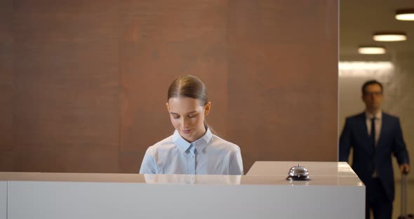 Young Businessman with Suitcase Signing Out of Hotel Leaving Card Key at Reception