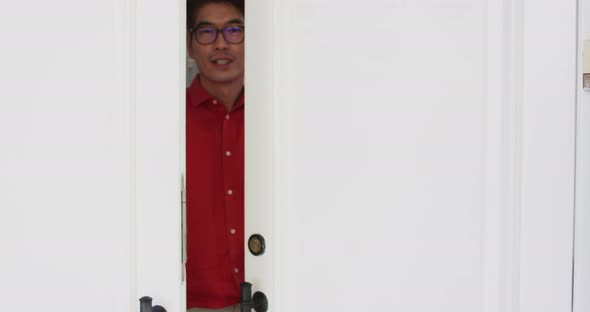 Happy asian man opening front door, smiling and greeting visitor to home