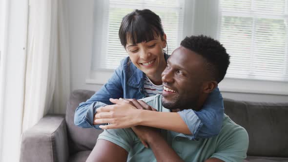 Portrait of happy diverse couple sitting on couch and embracing in living room