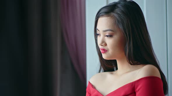 Medium Closeup Pensive Beautiful Asian Young Woman with Evening Makeup Looking on Window