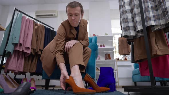 Wide Shot Thoughtful Confident Gay Man in Mustard Suit Trying on Dark Amber Highheels in Slow Motion
