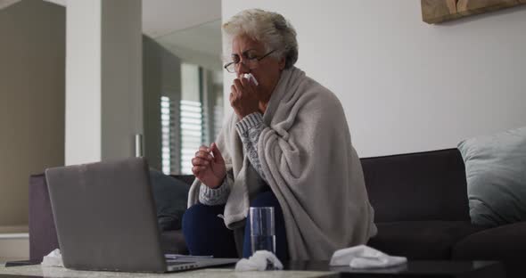 Sick african american senior woman coughing while having a video call on laptop at home