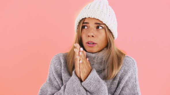 Lady in Sweater and Hat is Feeling Cold Trying to Warm Palms By Blowing on Them and Rubbing Together