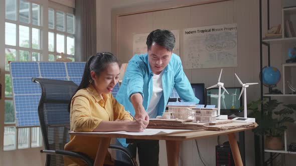Asian Man And Woman Helping Each Other Building The Model Of A Small House With Solar Panel