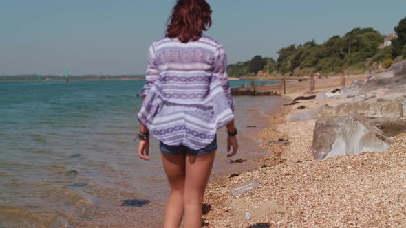 Young Woman Walks Along Beach and Picks Up Plastic Bottle