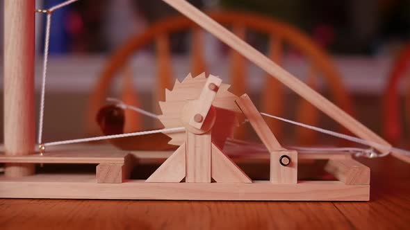 SLOW MOTION: Close up of a toy wooden trebuchet firing on a wooden table with a chair and counter in