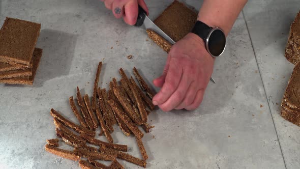 Overhead view as crusts are cut off dense rye bread on counter top