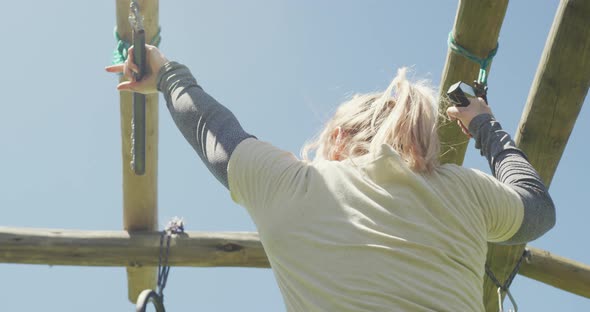 Fit caucasian female soldier hanging on trapeze bars on army obstacle course in sun