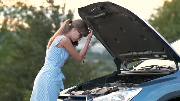 Upset young woman driver talking angrily on cell phone with assistance service near a broken car