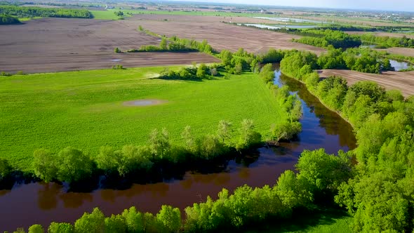 UHD aerial birds eye view of a small river flowing alongside some fields