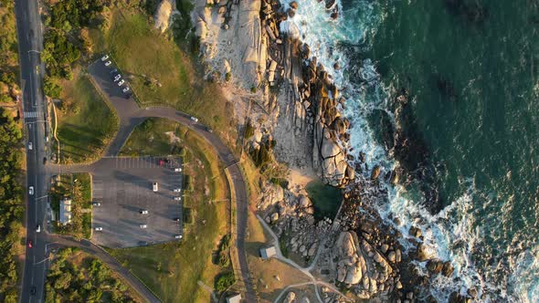 cars driving along coastal road near Maidens Cove Tidal Pool in Cape Town at sunset, aerial