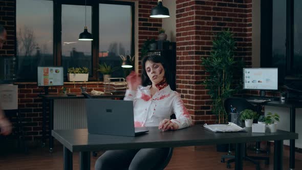 Spooky Zombie Sitting at Desk While Waving at Video Conference Call on Laptop