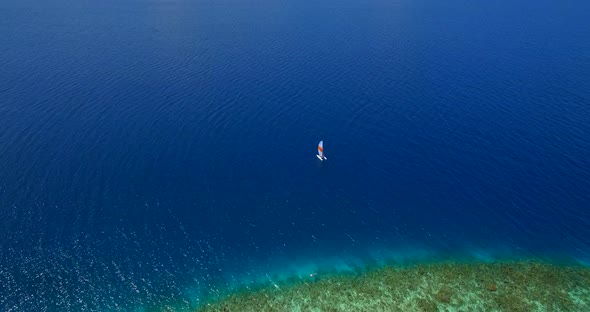 Aerial drone view of a man and woman sailing on a boat to a tropical island