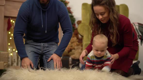 Mother, Father and Little Baby Sitting on the Floor in the Room with Christmas Decoration