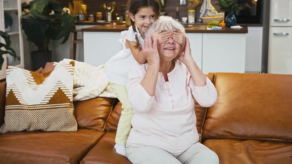 Grandmother Sitting on Couch Little Granddaughter Coming Up From Behind Closing Her Eyes Studio