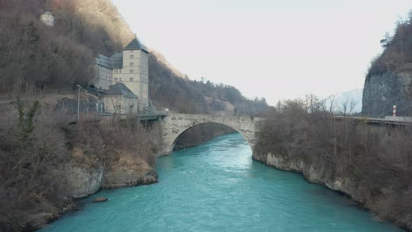 Aerial old bridge crossing a wild and blue river. A small castle is located nearby