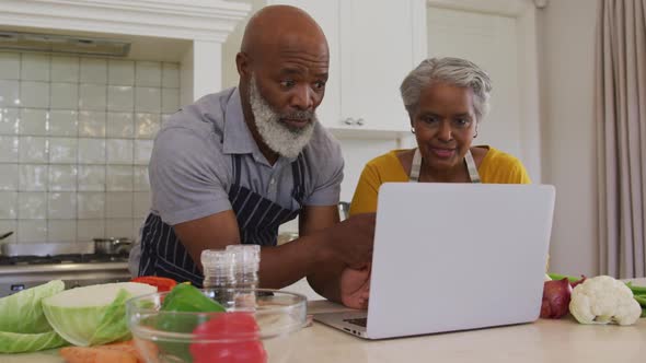 African american senior couple wearing aprons having a video call on laptop in the kitchen at home