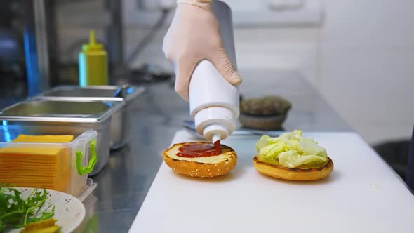 Cook adding ketchup on burger. Preparing burger on kitchen.