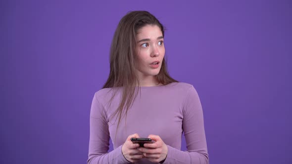 The Beautiful Young Woman Types on the Phone Looks to One Side Shocked Points with Her Index Finger