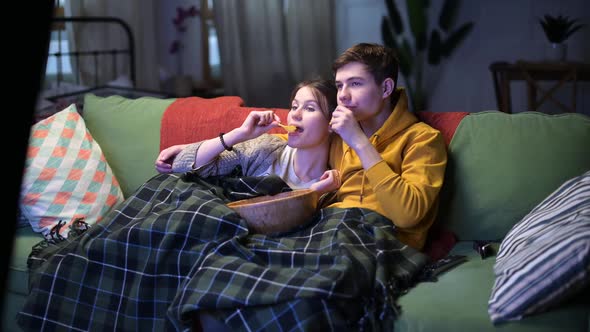 Young couple watching TV and eating chips in the evening on the sofa