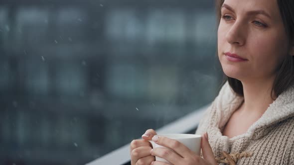 Woman Stays on Balcony During Snowfall with Cup of Hot Coffee or Tea