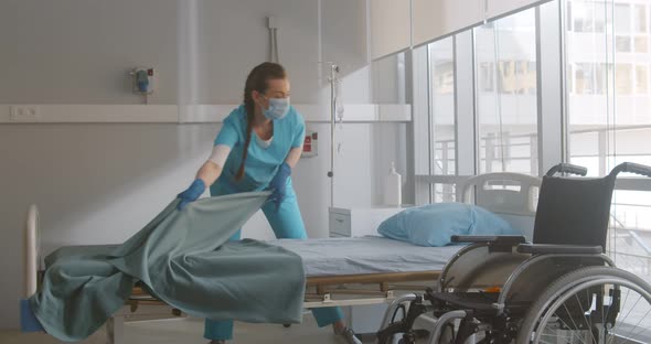 Portrait of Female Nurse Wearing Safety Mask and Gloves Changing Sheets in Hospital