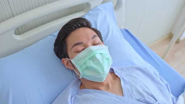 Asian young male patient wear protective facemask lying on bed, waiting for treatment from doctor.