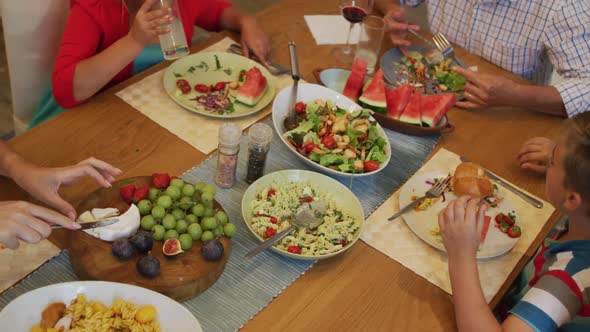 Parents, children and grandfather sitting at table eating during family meal